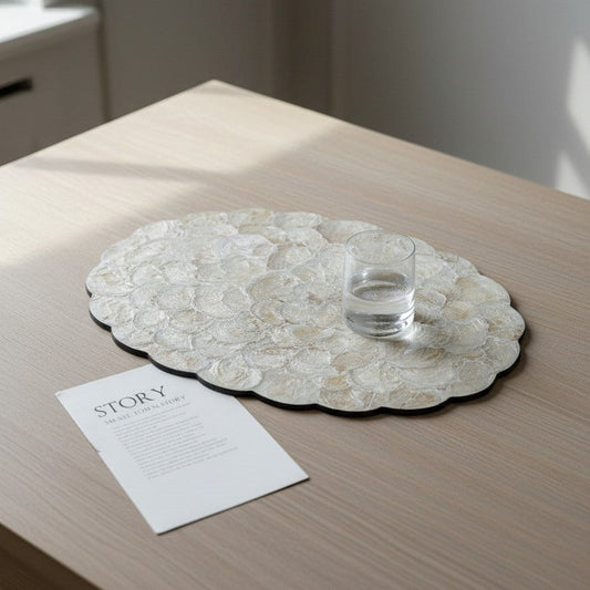 Round decorative placemat on a wooden table with a glass of water and a card.
