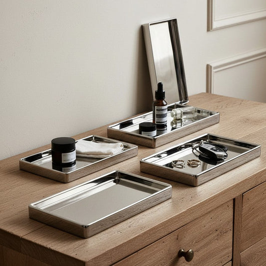 Set of silver trays on a wooden surface with a mirror and small items.