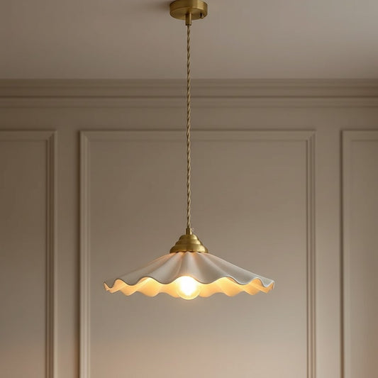 A single pendant light with a warm white scalloped glass shade and antique brass hardware, hanging against a beige paneled wall.