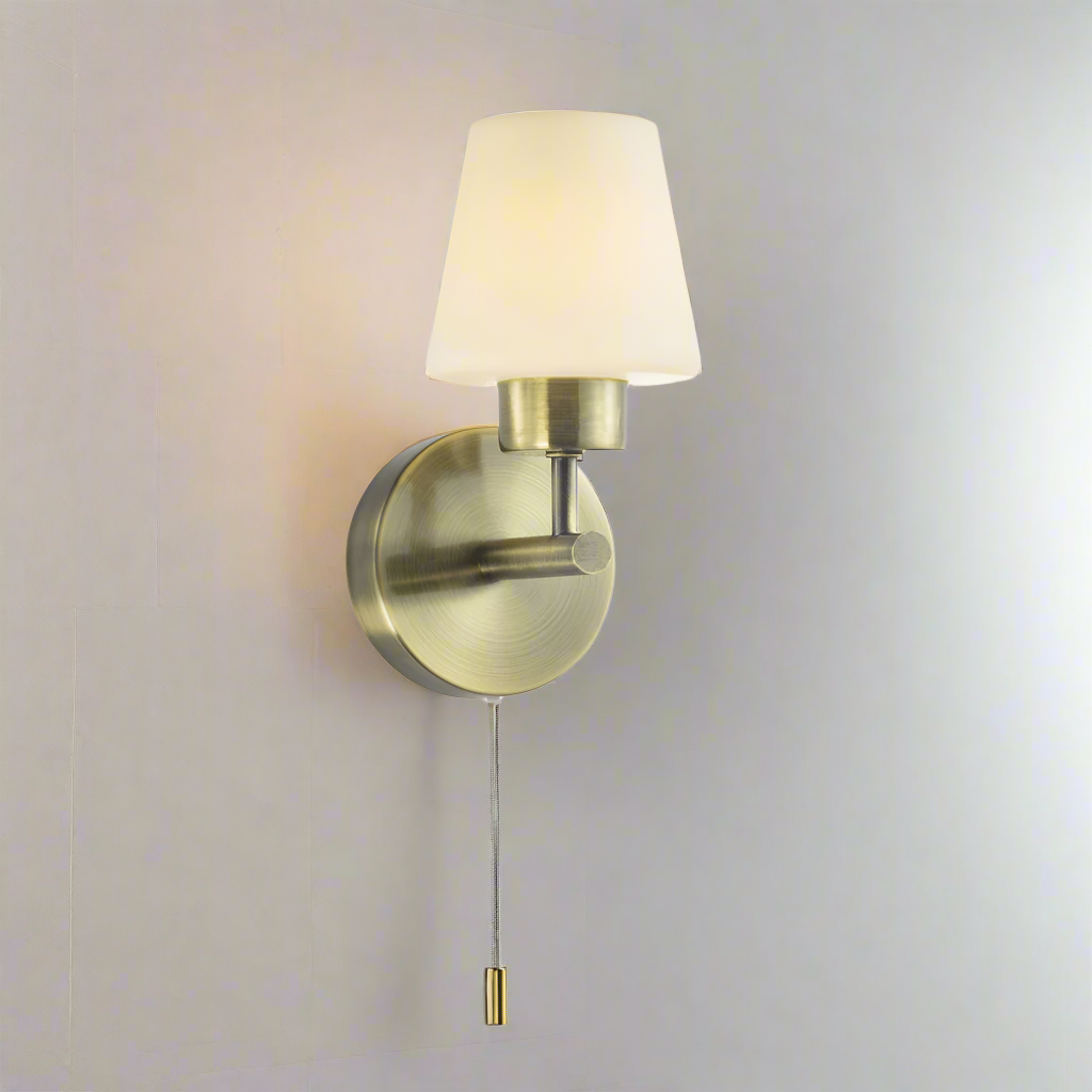 Wall-mounted lamp with brass fixture and white shade on a white background