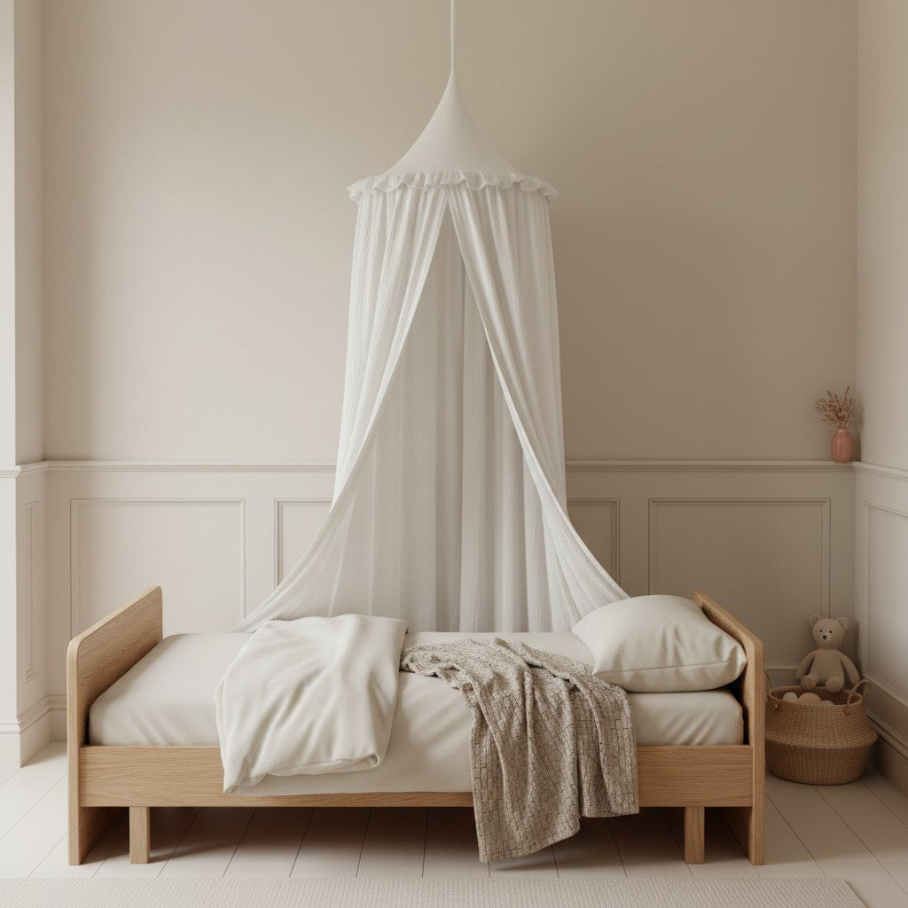 A light wood single bed with a white canopy tent draped over it, styled with white bedding and a textured beige throw blanket in a softly lit, neutral-toned nursery room.