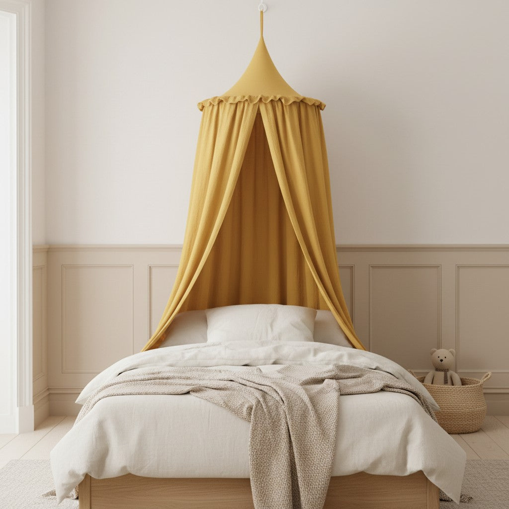 A mustard yellow fabric canopy bed cover hanging over a neatly made bed in a softly styled child's bedroom with cream bedding, a beige wall panel, and a small woven basket with a teddy bear.