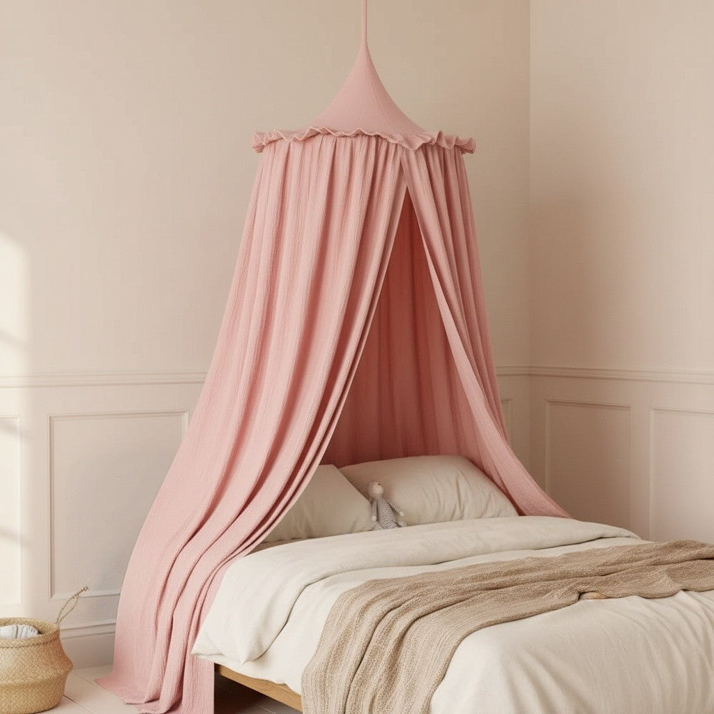 A dusty pink cotton canopy bed net hanging over a bed in a softly lit nursery with cream walls and wainscoting.