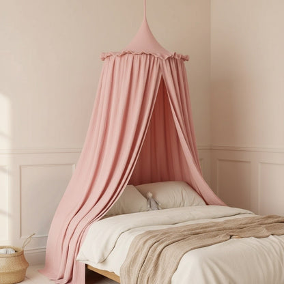 A dusty pink cotton canopy bed net hanging over a bed in a softly lit nursery with cream walls and wainscoting.