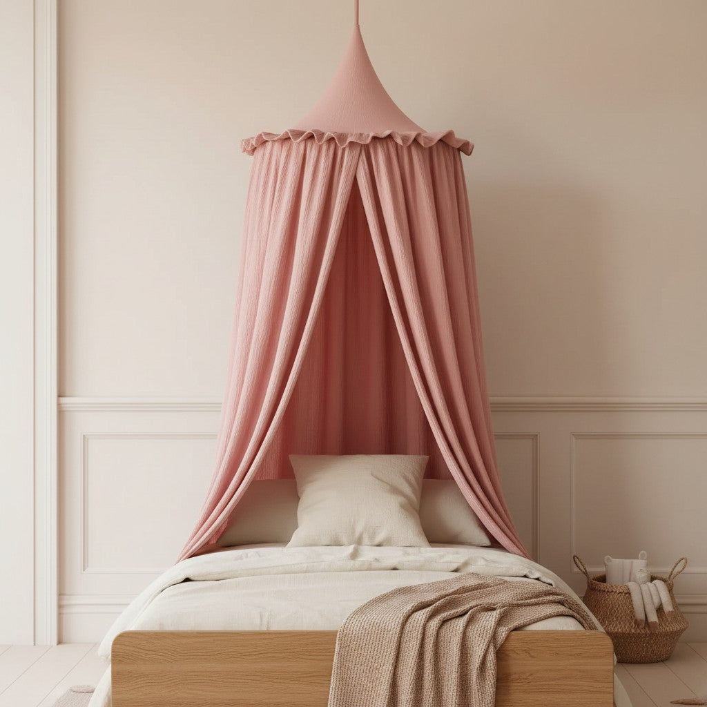 A pink fabric canopy bed curtain hanging over a wooden bed frame in a softly styled bedroom with cream bedding, a beige throw blanket, and a woven basket on the floor.