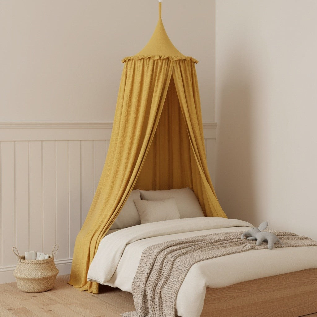 A mustard yellow fabric canopy bed in a styled children's bedroom. The bed is dressed in white bedding with a textured beige throw blanket, set against a cream wall with white wainscoting.