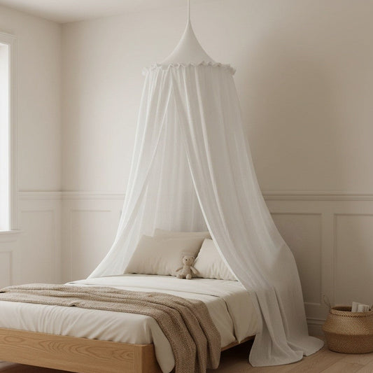 A white fabric canopy bed net hangs over a light wood bed in a softly lit neutral bedroom with cream walls, wainscoting, pale bedding, and a woven basket on the floor.