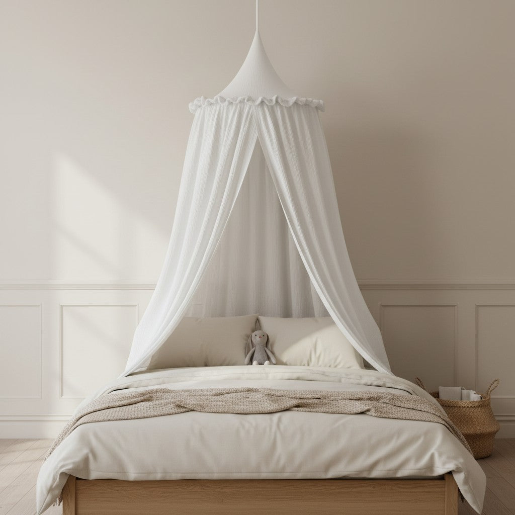 A white fabric canopy bed cover draped over a wooden bed frame with cream bedding, set in a softly lit, minimalist bedroom.