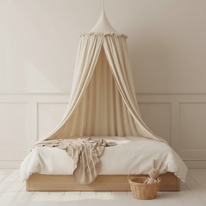 A beige fabric canopy bed curtain hanging over a wooden bed frame with white bedding, set in a softly lit nursery with a wicker basket and plush bunny nearby.