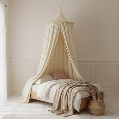 A cream-colored fabric canopy bed with draped curtains, styled on a wooden bed frame in a softly lit, neutral-toned nursery or bedroom setting.