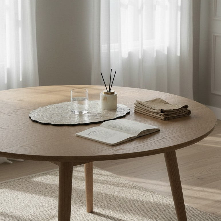 Round wooden table with a book, small plant, and decorative items in a bright room.