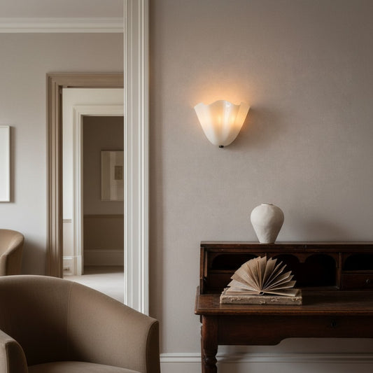 A warm, modern wall sconce with a fluted white glass shade mounted on a textured taupe-gray wall in a beautifully styled room with a dark wood console table, a white ceramic vase, and an open book.