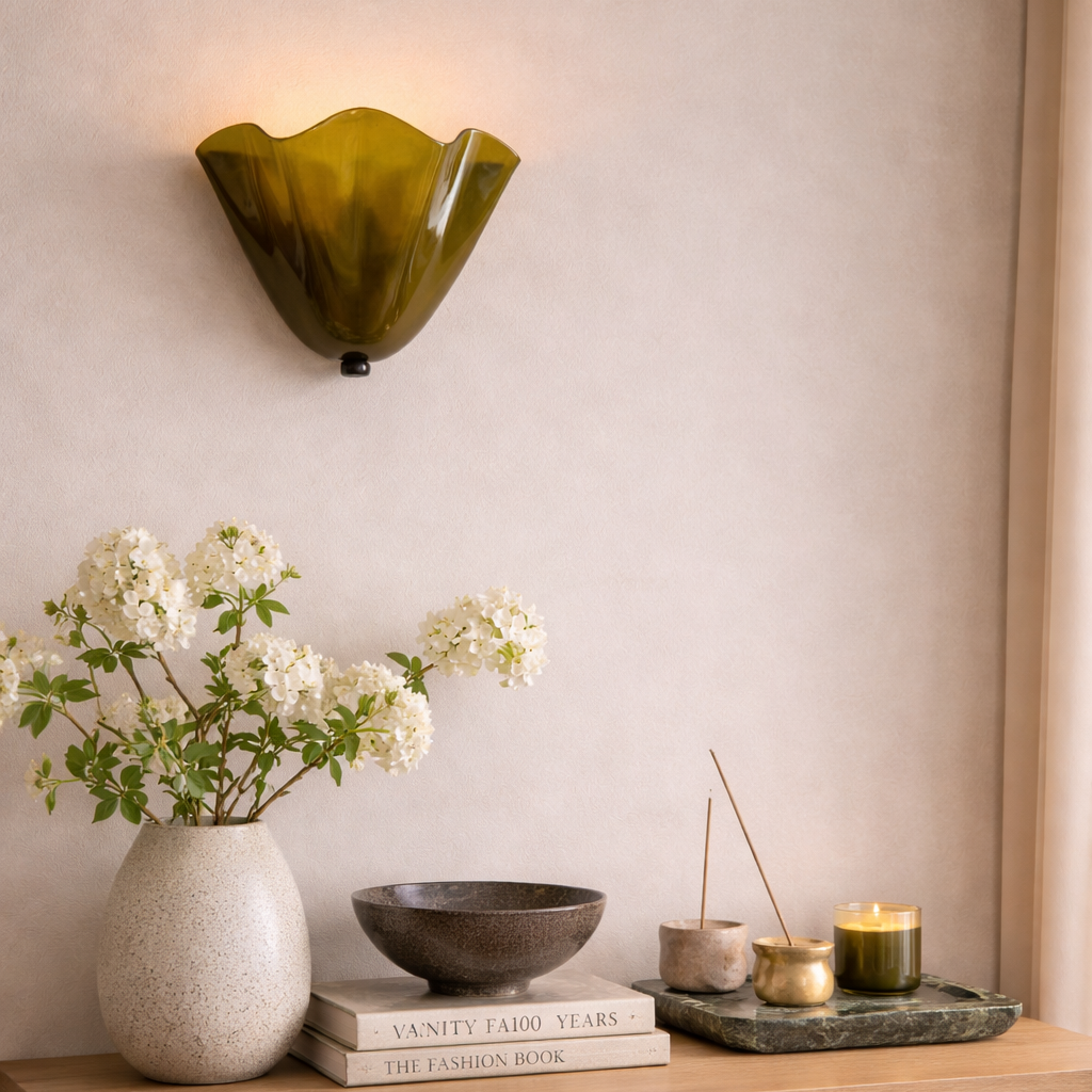 Decorative wall sconce, vase with flowers, books, and candles on a shelf against a neutral wall.
