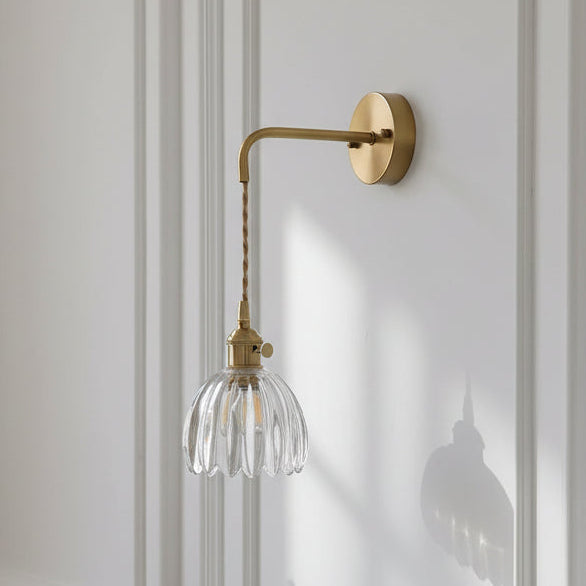 Wall-mounted lamp with a clear glass shade and gold fixture on a white wall.