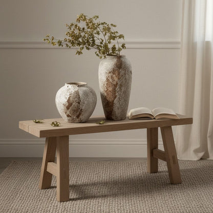 Two textured vases and an open book on a wooden bench against a neutral wall.
