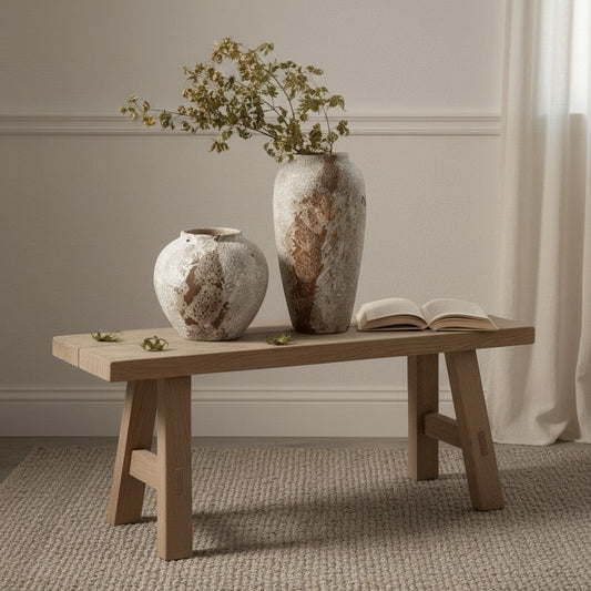 Two textured vases and an open book on a wooden bench against a neutral wall.