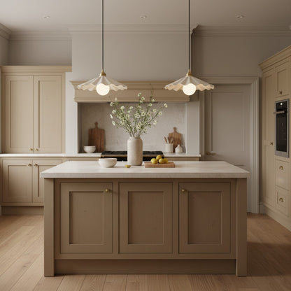 A styled kitchen interior with a central island in muted taupe, cream cabinetry, a white marble countertop, pendant lights, and a vase of white flowers on the counter.