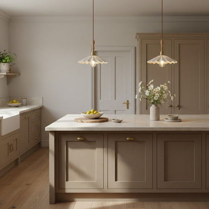 A modern kitchen interior with a central island in taupe-brown shaker-style cabinets, a white marble countertop, two hanging pendant lights, and light wood flooring.