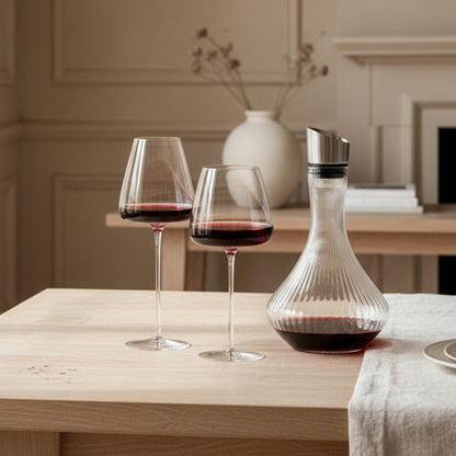 Two wine glasses with red wine and a decanter on a wooden table in a elegant room.