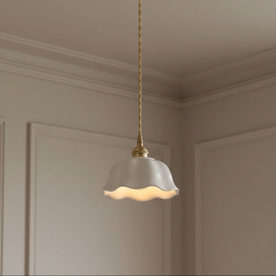 A hanging pendant light with a white fluted glass shade and a twisted brass cord, shown installed in a cream-colored room corner.