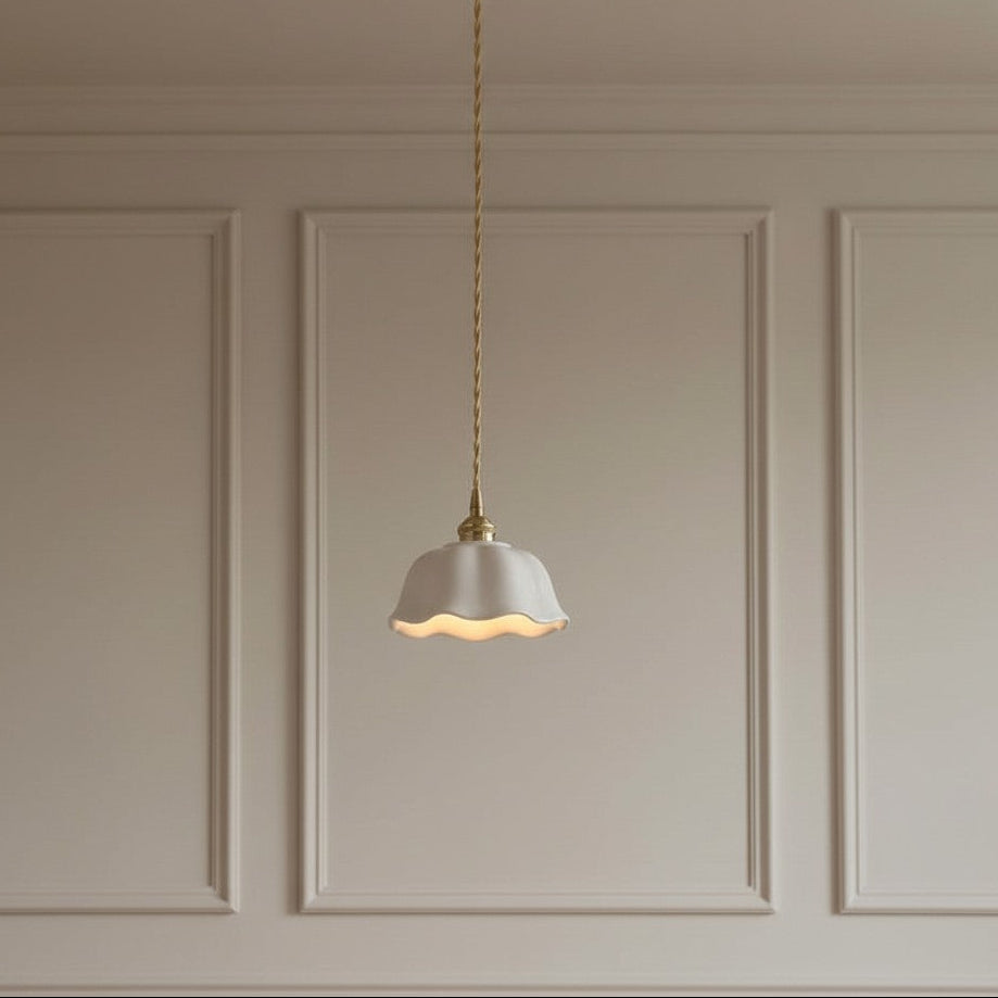 A single pendant light with a white scalloped glass shade and a gold-toned brass ceiling mount and twisted cord, hanging against a beige paneled wall.