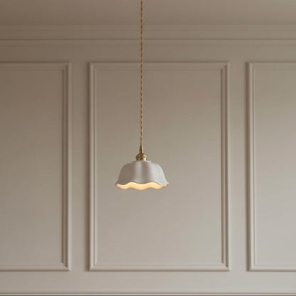 A single pendant light with a white scalloped glass shade and a gold-toned brass ceiling mount and twisted cord, hanging against a beige paneled wall.