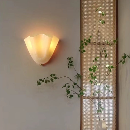 Wall-mounted light fixture on a wall with a plant and woven screen in the background