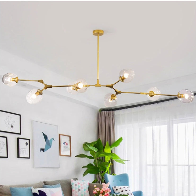 Modern living room with a gold chandelier, colorful decor, and a plant.